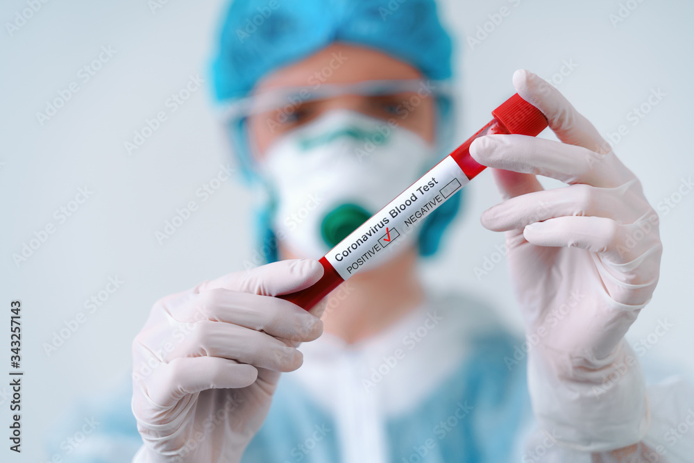 Positive COVID-19 test. Virologist in a medical mask and protective suit holds a test tube with positive blood sample Positive COVID-19 test. Virologist in a medical mask and protective suit holds a test tube with positive blood sample