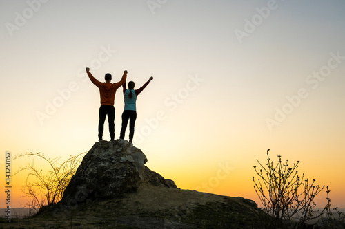 Obraz na plátně Man and woman hikers standing on a big stone at sunset in mountains