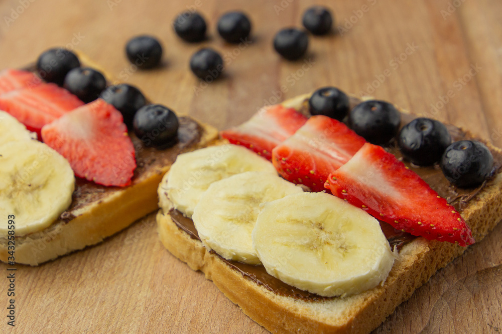 Breakfast with fruit sandwich with strawberry, banana, blueberry on a wooden board. Concept of healthy meal. Breakfast with fruit sandwich with strawberry, banana, blueberry on a wooden board. Concept of healthy meal.
