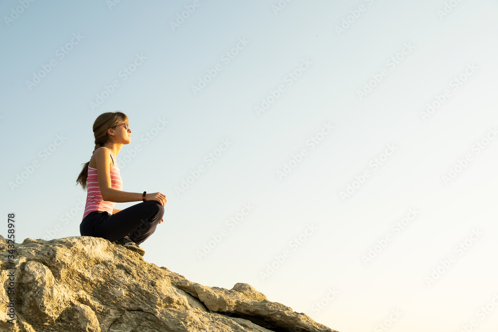 Woman hiker sitting on a steep big rock enjoying warm summer day. Young female climber resting during sports activity in nature. Active recreation in nature concept. Woman hiker sitting on a steep big rock enjoying warm summer day. Young female climber resting during sports activity in nature. Active recreation in nature concept.