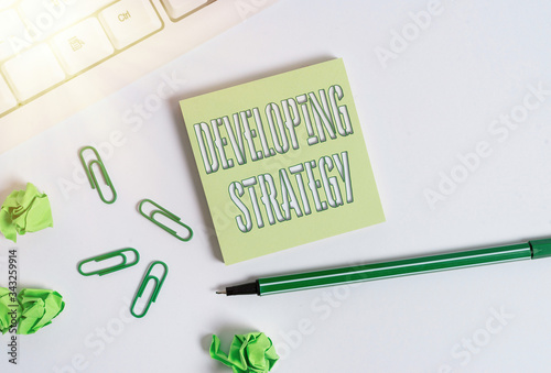 Text sign showing Developing Strategy. Business photo showcasing Organizations Process Changes to reach Objectives Square empty green note paper with pencil on the white background and pc keyboard photo