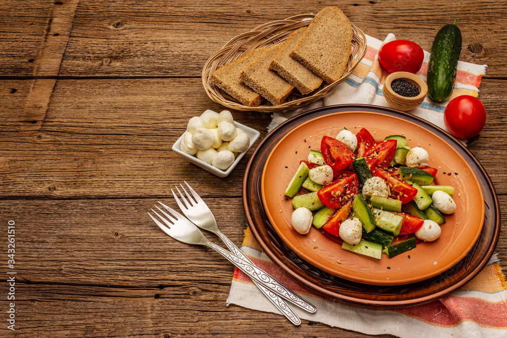 Fresh salad from tomato, cucumber and baby mozzarella. Sunny lunch with crusty bread Fresh salad from tomato, cucumber and baby mozzarella. Sunny lunch with crusty bread