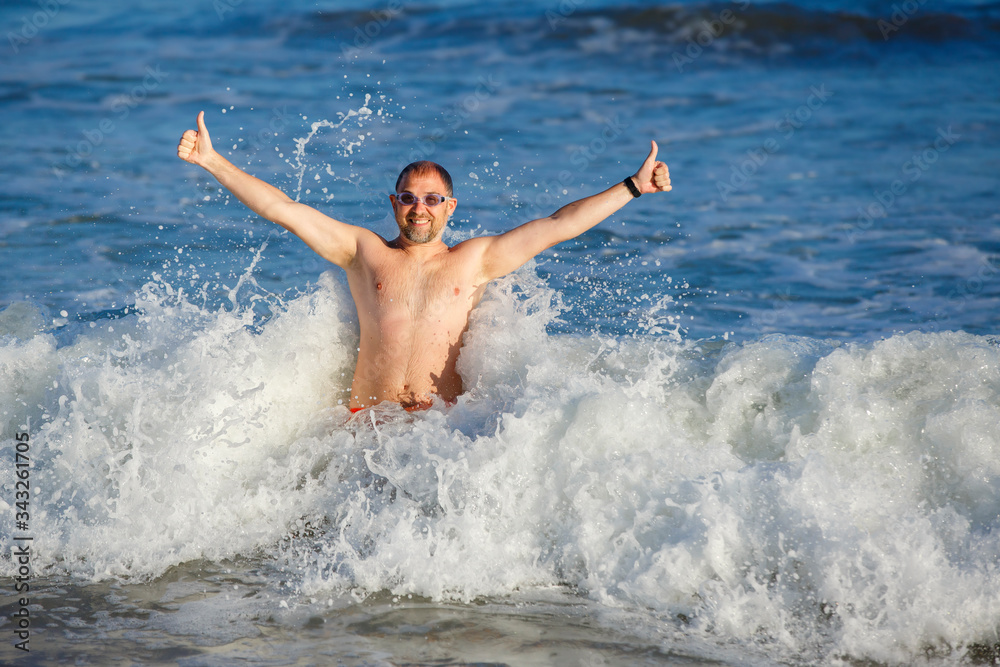 Young man splashing in ocean waves. Ocean and water fun for adults