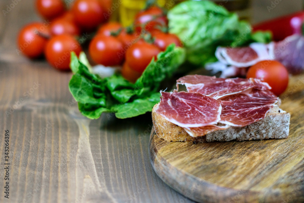 Homemade sandwitch of bread and fresh ham on the wooden cutting board. Vegatables prepared for snack. Healthy mediterranean food. Homemade sandwitch of bread and fresh ham on the wooden cutting board. Vegatables prepared for snack. Healthy mediterranean food.