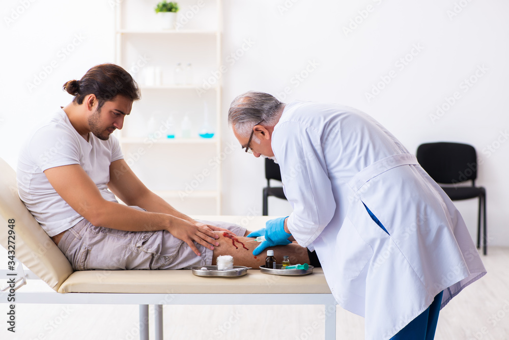Leg injured man visiting old doctor in first aid concept Leg injured man visiting old doctor in first aid concept