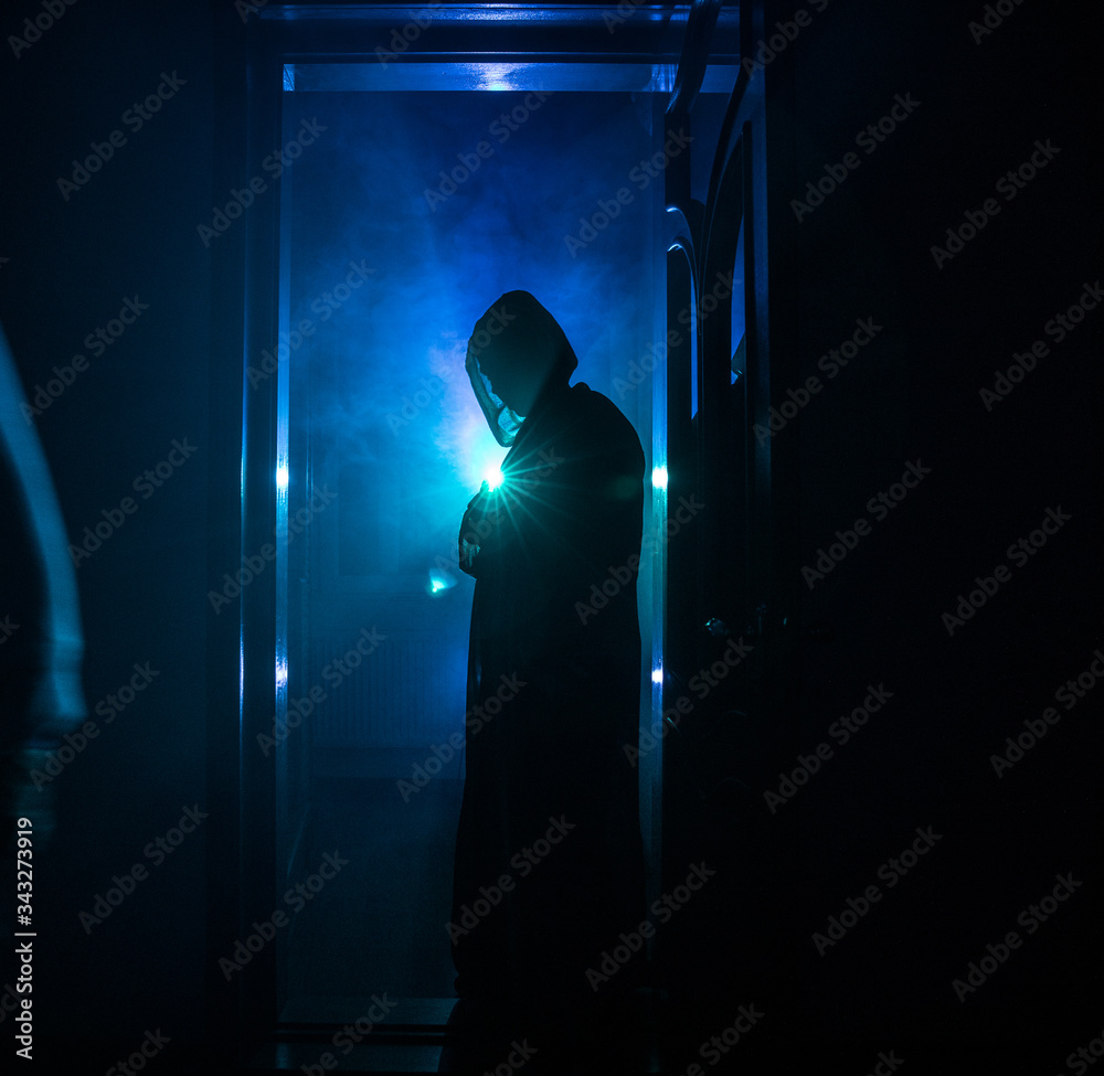 Silhouette of an unknown shadow figure on a door through a closed glass door. The silhouette of a human in front of a window at night. Scary scene halloween concept of blurred silhouette of maniac.