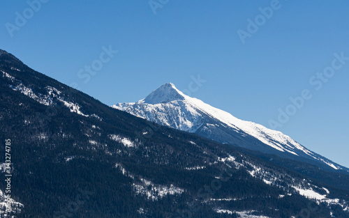 close-up view of the mountain peak with trees and snow on it sunny spring day.