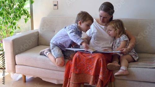 Young mother reading a book to her two children and having fun at home during quarantine