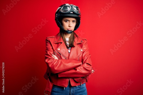 Young beautiful brunette motocyclist woman wearing motorcycle helmet and red jacket skeptic and nervous, disapproving expression on face with crossed arms. Negative person. © Krakenimages.com