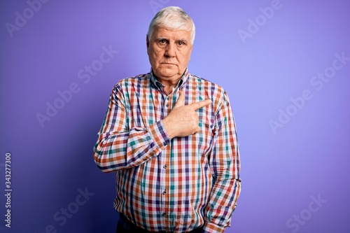Senior handsome hoary man wearing casual colorful shirt over isolated purple background Pointing with hand finger to the side showing advertisement, serious and calm face