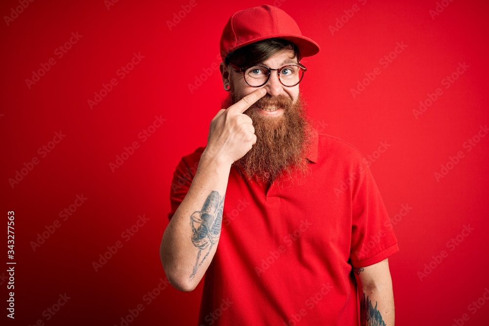 Young handsome delivery man wearing glasses and red cap over isolated background Pointing with hand finger to face and nose, smiling cheerful. Beauty concept Young handsome delivery man wearing glasses and red cap over isolated background Pointing with hand finger to face and nose, smiling cheerful. Beauty concept