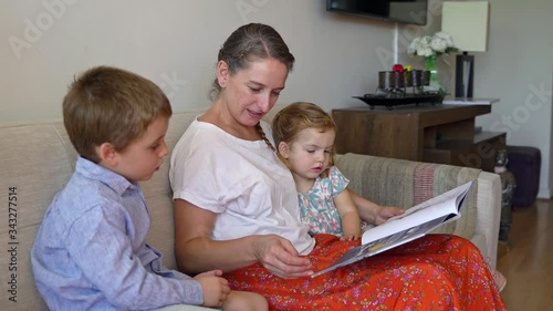Young mother reading a book to her two children and having fun at home during quarantine