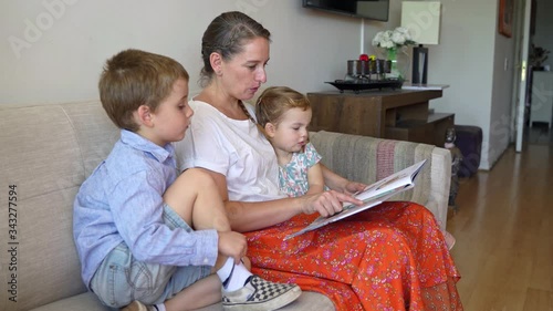 Young mother reading a book to her two children and having fun at home during quarantine