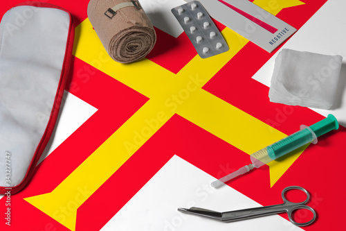 Guernsey flag with first aid medical kit on wooden table background. National healthcare system concept, medical theme.