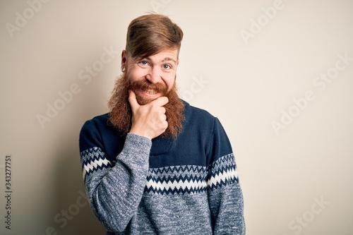 Handsome Irish redhead man with beard wearing winter sweater over isolated background looking confident at the camera smiling with crossed arms and hand raised on chin. Thinking positive.