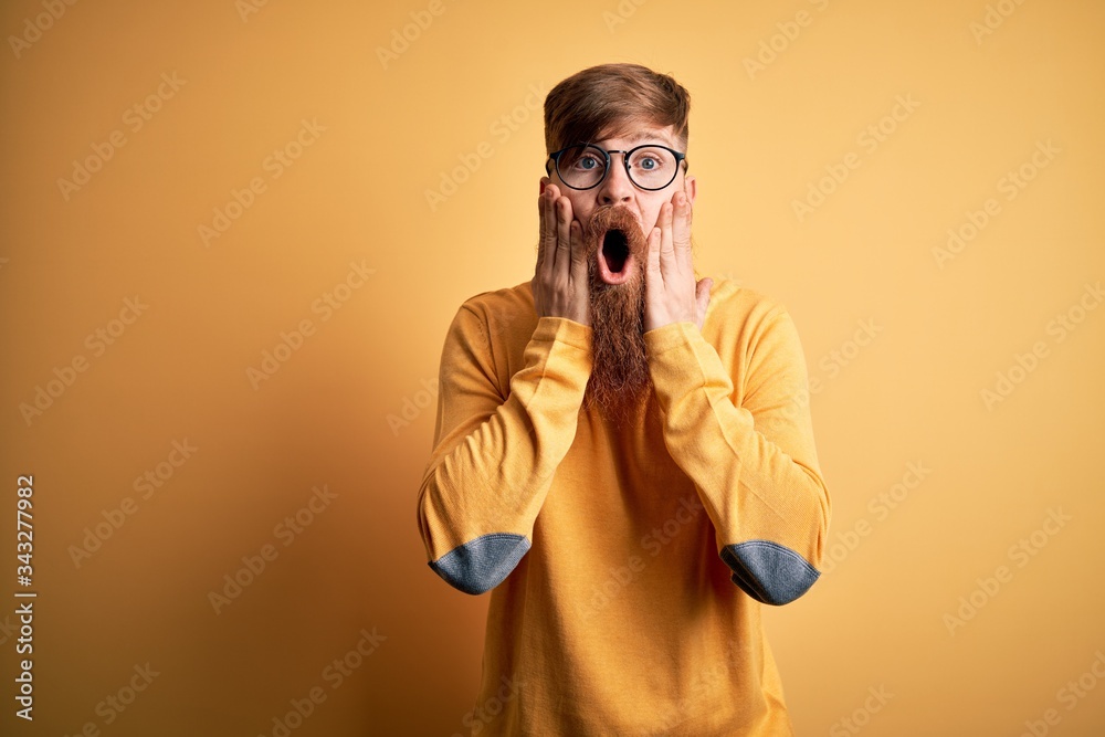 Handsome Irish redhead man with beard wearing glasses over yellow isolated background afraid and shocked, surprise and amazed expression with hands on face Handsome Irish redhead man with beard wearing glasses over yellow isolated background afraid and shocked, surprise and amazed expression with hands on face