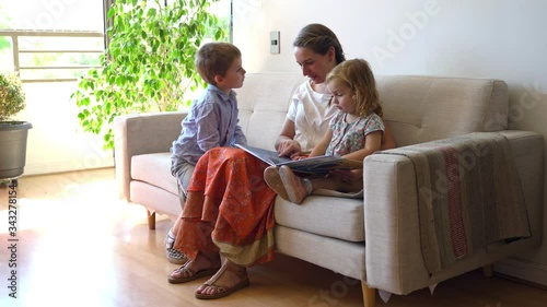 Young mother reading a book to her two children and having fun at home during quarantine