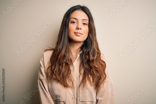Young beautiful brunette woman wearing casual shirt standing over white background Relaxed with serious expression on face. Simple and natural looking at the camera. © Krakenimages.com