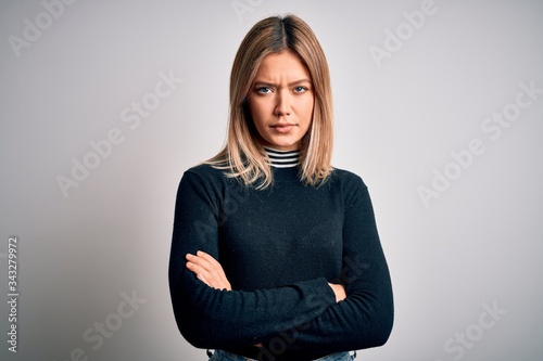 Young beautiful blonde woman with blue eyes standing over white isolated background skeptic and nervous, disapproving expression on face with crossed arms. Negative person.