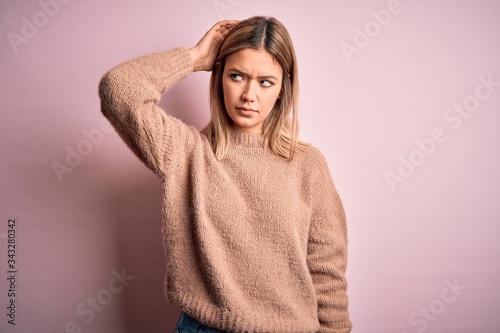 Young beautiful blonde woman wearing winter wool sweater over pink isolated background confuse and wondering about question. Uncertain with doubt, thinking with hand on head. Pensive concept.