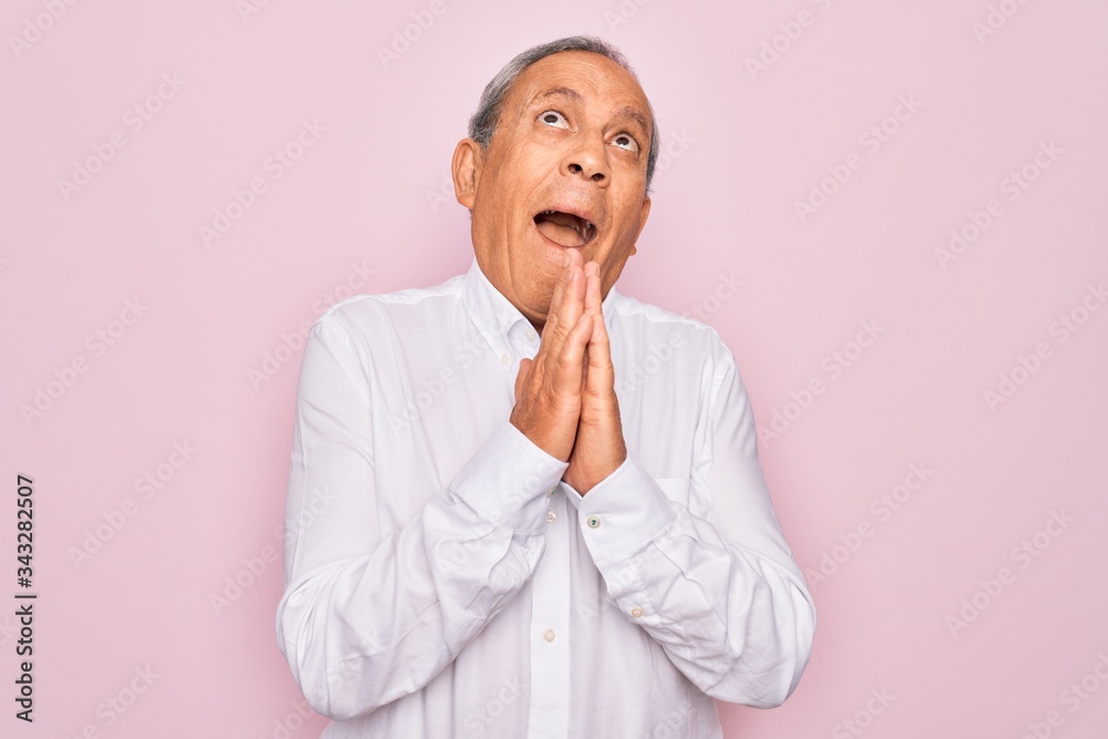Senior handsome grey-haired man wearing elegant shirt over isolated pink background begging and praying with hands together with hope expression on face very emotional and worried. Begging. Senior handsome grey-haired man wearing elegant shirt over isolated pink background begging and praying with hands together with hope expression on face very emotional and worried. Begging.