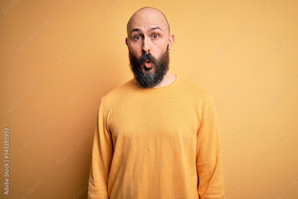 Handsome bald man with beard wearing casual sweater standing over yellow background afraid and shocked with surprise expression, fear and excited face.