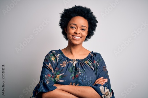 Young beautiful African American afro woman with curly hair wearing casual floral dress happy face smiling with crossed arms looking at the camera. Positive person.