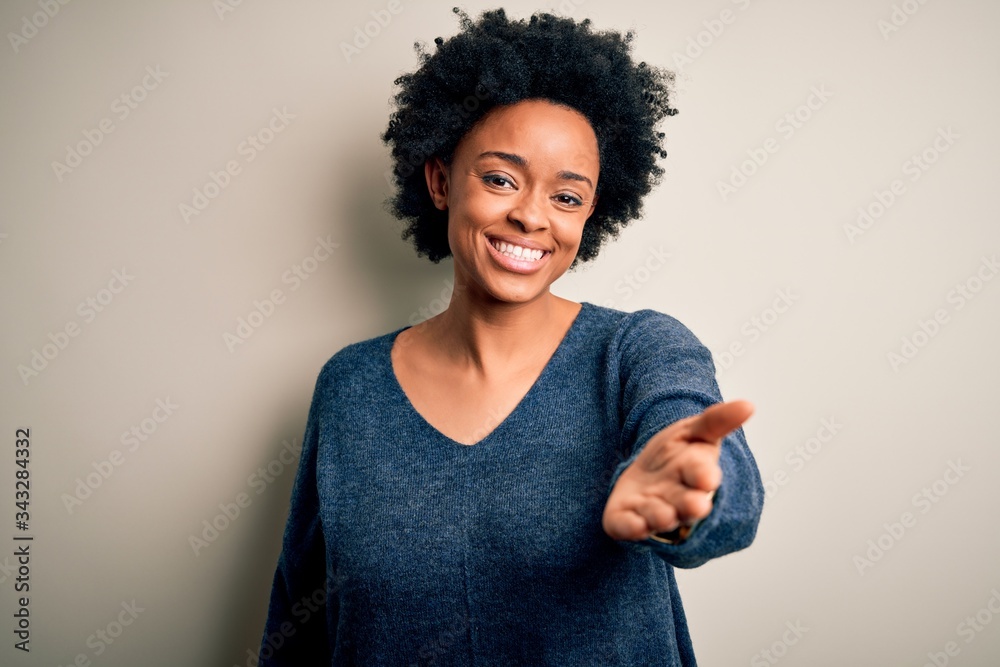 Young beautiful African American afro woman with curly hair wearing casual sweater smiling cheerful offering palm hand giving assistance and acceptance. Young beautiful African American afro woman with curly hair wearing casual sweater smiling cheerful offering palm hand giving assistance and acceptance.