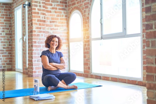 Middle age beautiful sportswoman wearing sportswear sitting on mat practicing yoga at home happy face smiling with crossed arms looking at the camera. Positive person.