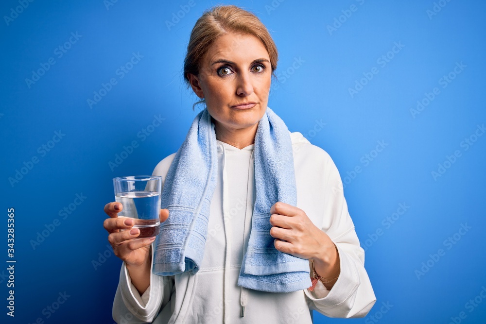 Middle age beautiful blonde sportswoman wearing towel drinking glass of water to refreshment with a confident expression on smart face thinking serious Middle age beautiful blonde sportswoman wearing towel drinking glass of water to refreshment with a confident expression on smart face thinking serious