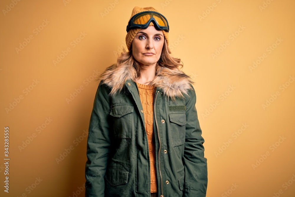 Middle age beautiful blonde skier woman wearing snow sportwear and ski goggles Relaxed with serious expression on face. Simple and natural looking at the camera. Middle age beautiful blonde skier woman wearing snow sportwear and ski goggles Relaxed with serious expression on face. Simple and natural looking at the camera.