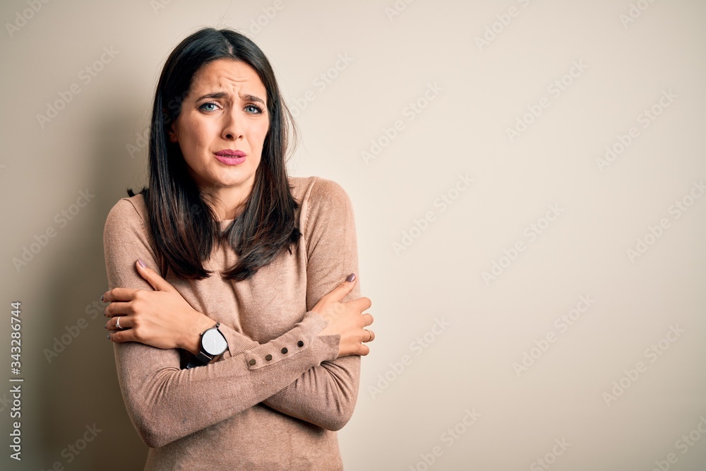 Obraz premium Young brunette woman with blue eyes wearing casual sweater over isolated white background shaking and freezing for winter cold with sad and shock expression on face
