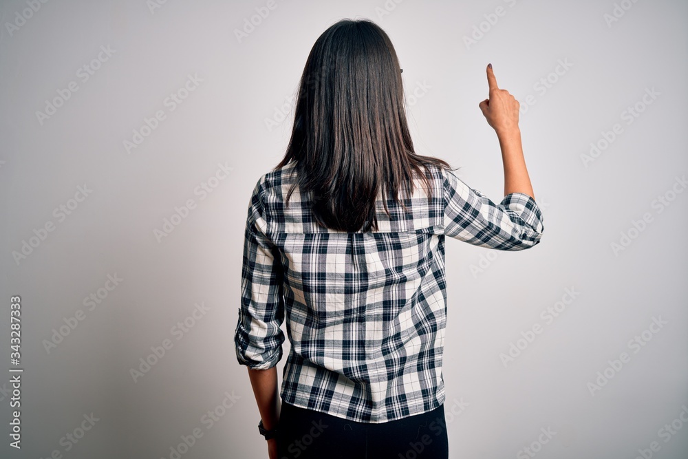Young brunette woman with blue eyes wearing casual shirt and glasses over white background Posing backwards pointing ahead with finger hand Young brunette woman with blue eyes wearing casual shirt and glasses over white background Posing backwards pointing ahead with finger hand