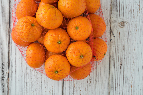 Small clementine oranges in a red mesh bag on a whitewashed wood background
