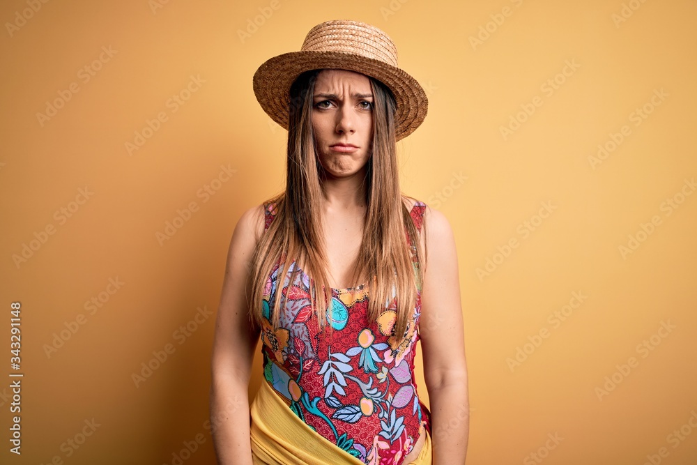 Young beautiful blonde woman wearing swimsuit and summer hat over yellow background depressed and worry for distress, crying angry and afraid. Sad expression.