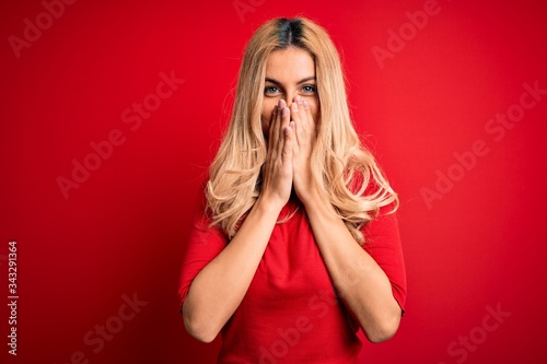 фотографія Young beautiful blonde woman wearing casual t-shirt standing over isolated red b