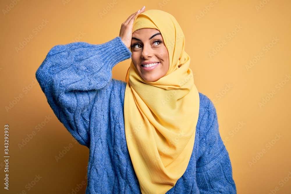 Young beautiful brunette muslim woman wearing arab hijab over isolated yellow background smiling confident touching hair with hand up gesture, posing attractive and fashionable Young beautiful brunette muslim woman wearing arab hijab over isolated yellow background smiling confident touching hair with hand up gesture, posing attractive and fashionable