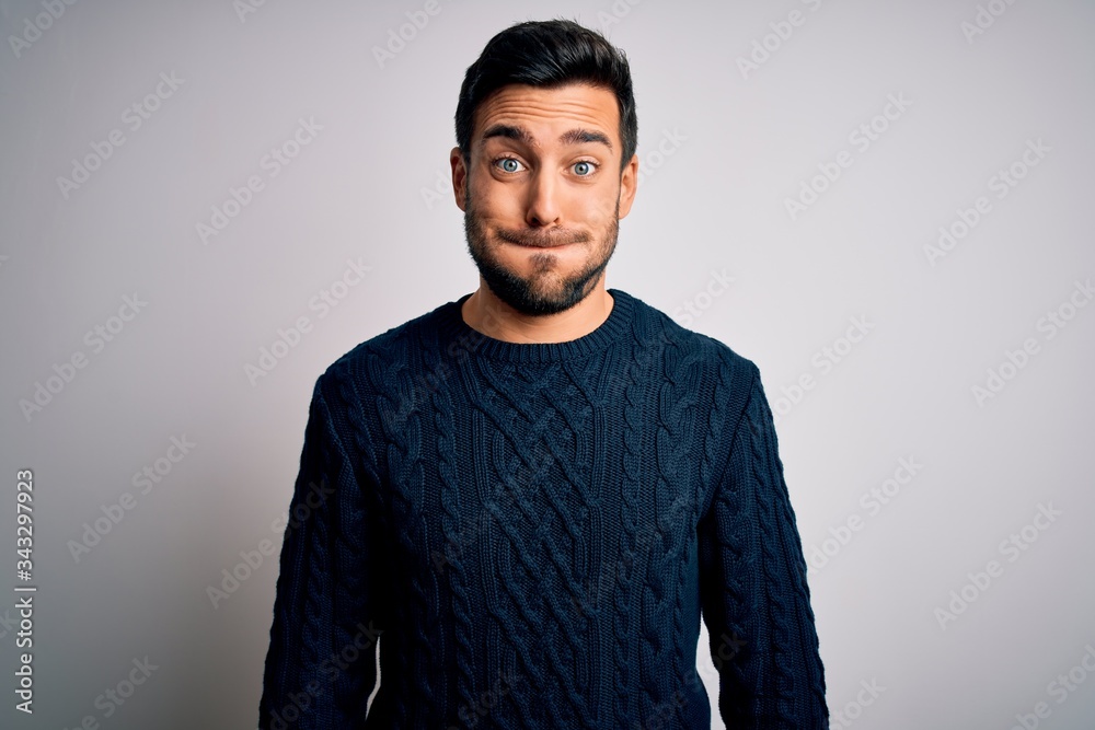 Obraz premium Young handsome man with beard wearing casual sweater standing over white background puffing cheeks with funny face. Mouth inflated with air, crazy expression.