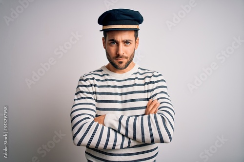 Young handsome sailor man with beard wearing navy striped uniform and captain hat skeptic and nervous, disapproving expression on face with crossed arms. Negative person. photo