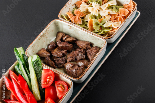 Sport nutrition with pasta, fried liver and fresh vegetables in plate on black background. Healthy food, dieting, top view