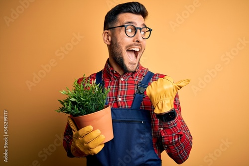 Fotografiet Young gardener man wearing working apron gardening plat for hobby over yellow ba
