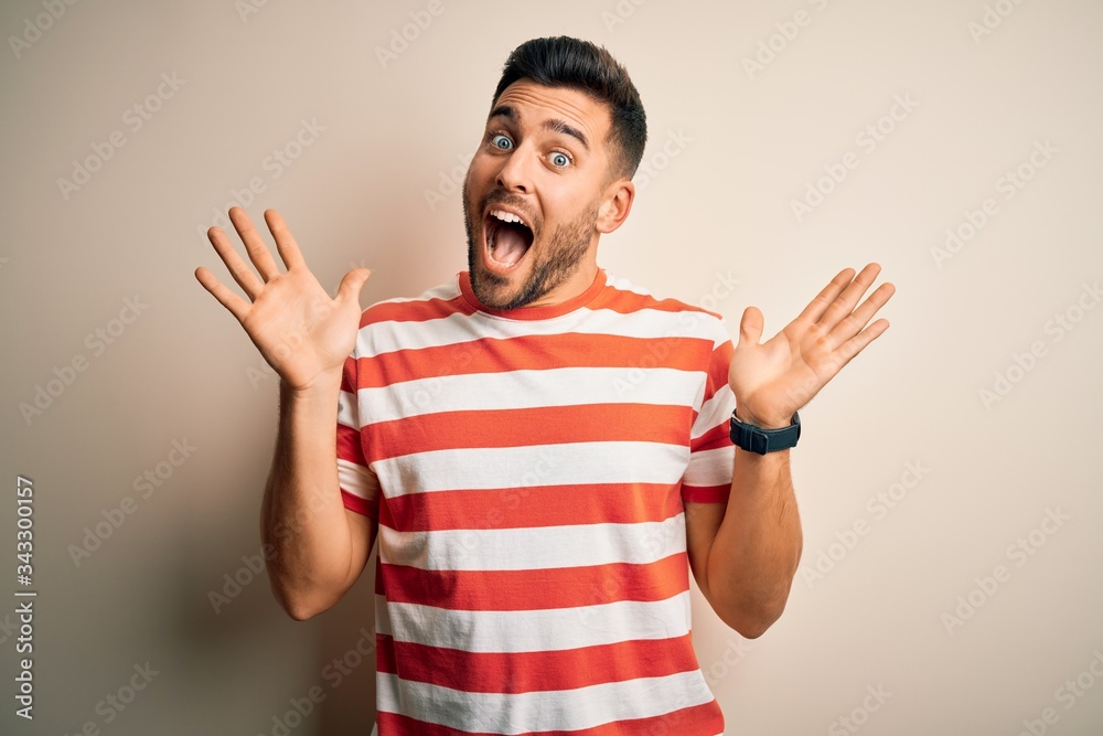 Young handsome man wearing casual striped t-shirt standing over isolated white background celebrating crazy and amazed for success with arms raised and open eyes screaming excited. Winner concept Young handsome man wearing casual striped t-shirt standing over isolated white background celebrating crazy and amazed for success with arms raised and open eyes screaming excited. Winner concept