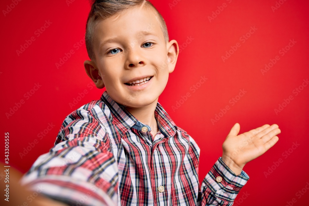 Close up of young little caucasian kid with blue eyes taking a selfie photo over red background very happy and excited, winner expression celebrating victory screaming with big smile and raised hands Close up of young little caucasian kid with blue eyes taking a selfie photo over red background very happy and excited, winner expression celebrating victory screaming with big smile and raised hands