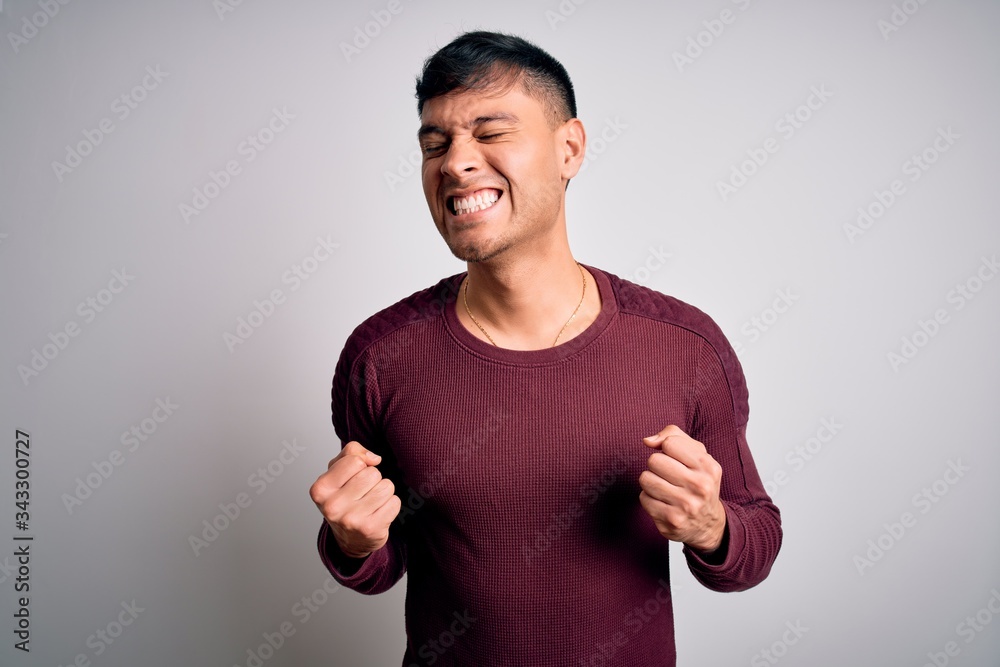 Young handsome hispanic man wearing casual shirt standing over white isolated background excited for success with arms raised and eyes closed celebrating victory smiling. Winner concept. Young handsome hispanic man wearing casual shirt standing over white isolated background excited for success with arms raised and eyes closed celebrating victory smiling. Winner concept.