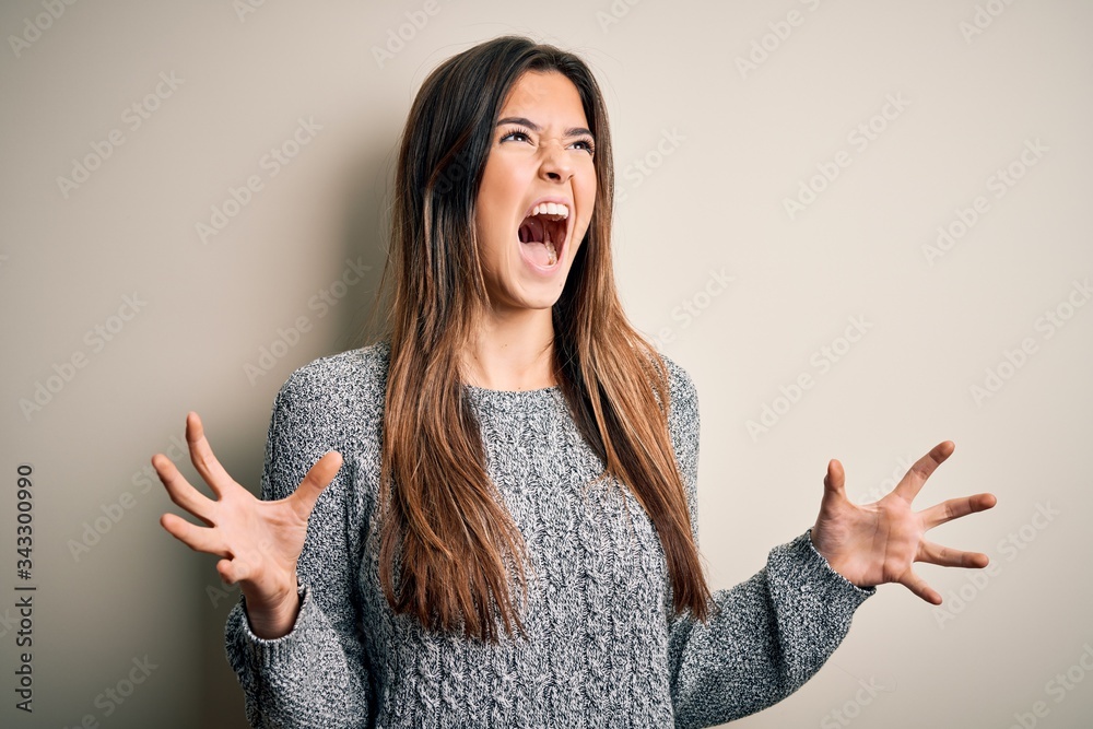 Young beautiful girl wearing casual sweater standing over isolated white background crazy and mad shouting and yelling with aggressive expression and arms raised. Frustration concept. Young beautiful girl wearing casual sweater standing over isolated white background crazy and mad shouting and yelling with aggressive expression and arms raised. Frustration concept.