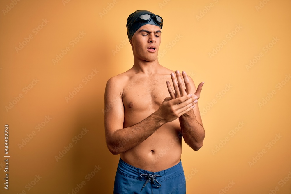 Young handsome man shirtless wearing swimsuit and swim cap over isolated yellow background Suffering pain on hands and fingers, arthritis inflammation
