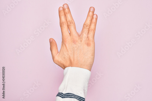 Hand of caucasian young man showing fingers over isolated pink background greeting doing Vulcan salute, showing back of the hand and fingers, freak culture