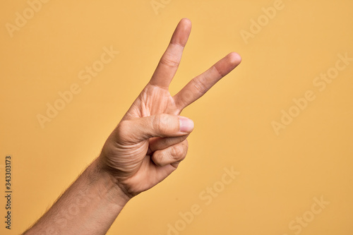 Hand of caucasian young man showing fingers over isolated yellow background counting number 2 showing two fingers, gesturing victory and winner symbol photo