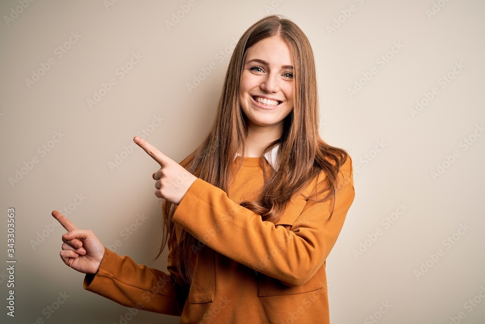 Young beautiful redhead woman wearing casual sweater over isolated white background smiling and looking at the camera pointing with two hands and fingers to the side. Young beautiful redhead woman wearing casual sweater over isolated white background smiling and looking at the camera pointing with two hands and fingers to the side.