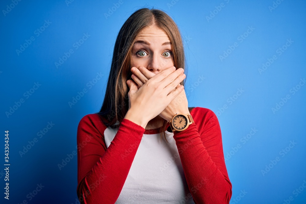 Young beautiful redhead woman wearing casual t-shirt over isolated blue background shocked covering mouth with hands for mistake. Secret concept. Young beautiful redhead woman wearing casual t-shirt over isolated blue background shocked covering mouth with hands for mistake. Secret concept.